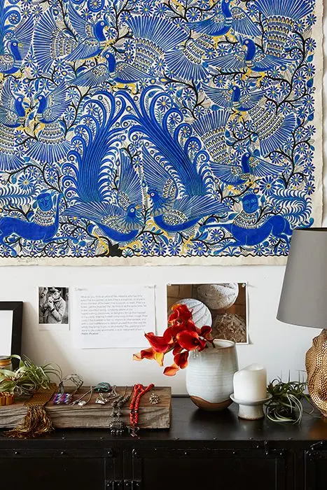 Blue embroidered textile of birds above a console with ceramics, flowers and jewelry